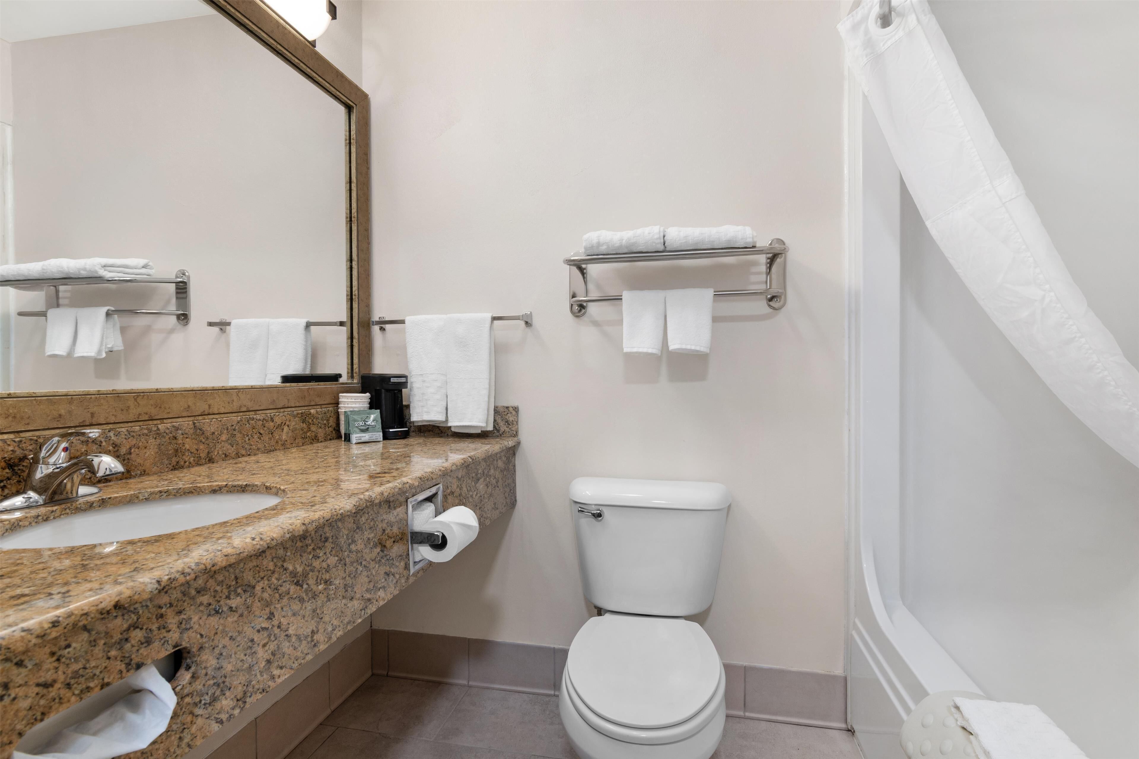 A bathroom with a granite countertop sink, a toilet, and a towel rack.