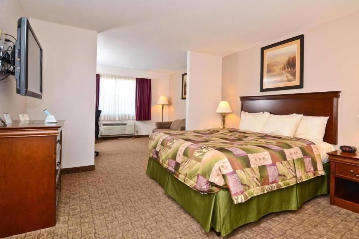 A hotel room with a bed, a desk, a chair, a lamp, and a painting on the wall.