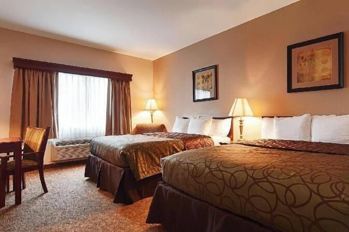 A hotel room with two beds, a desk, a chair, and two lamps.