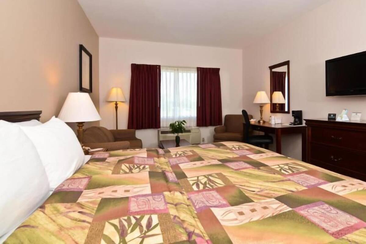 A hotel room with a bed, two chairs, a desk, a television, and a window with curtains.