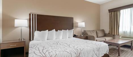 A hotel room with a large bed, two bedside lamps, a sofa, a coffee table, and a window with curtains.