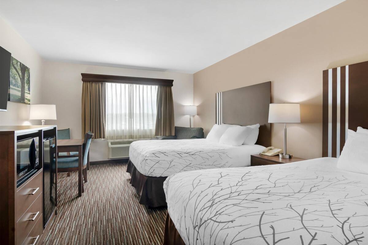 A hotel room with two beds, a desk, a chair, a TV, and a window with curtains.