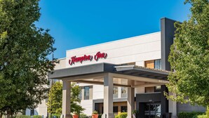 Ein Hampton Inn Hotel mit moderner Fassade, überdachter Eingangspartei und Blumentöpfen.