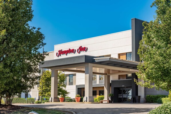 A Hampton Inn hotel with a modern facade, a covered entrance, and potted plants.