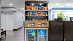 Ein Getränkeautomat mit Snacks und Getränken, eine Bank und ein Empfangsbereich mit Pflanze und Telefon.
