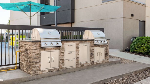 Ein Grillbereich im Freien mit Steinunterbau und mehreren Grillstationen, gelegen in einem Innenhof mit einem Gebäude im Hintergrund.