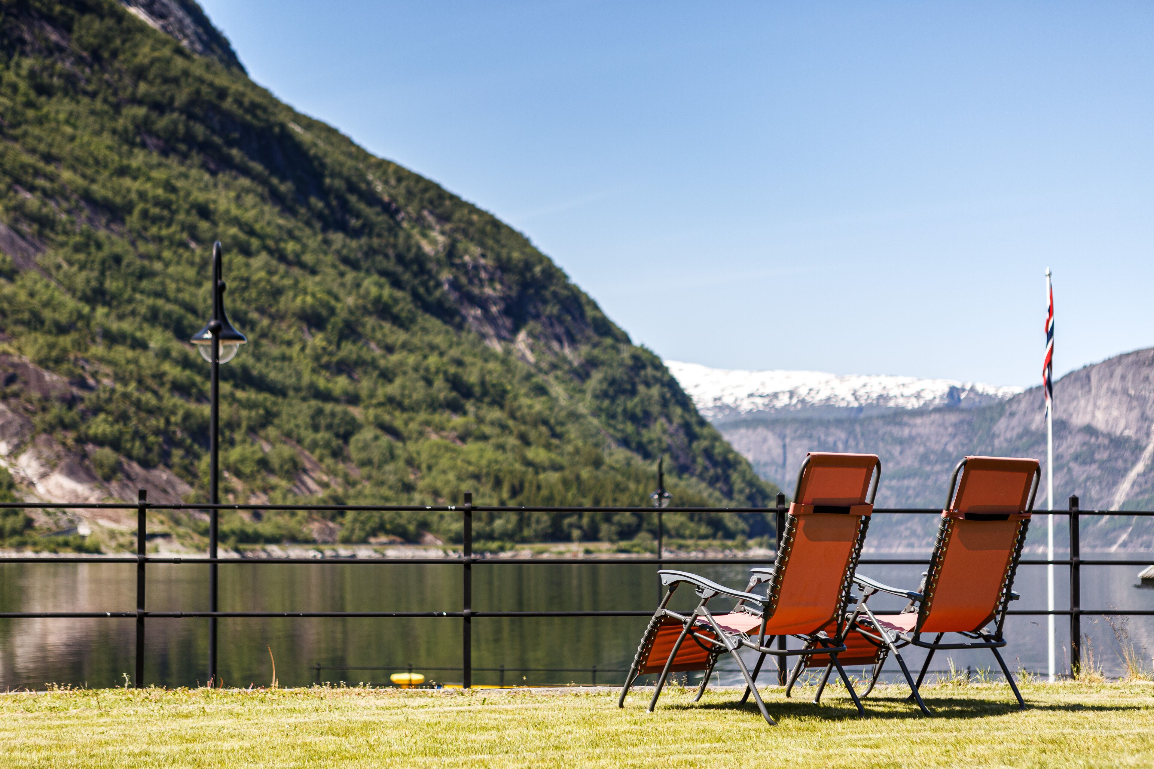 Two orange folding chairs by a lake with a mountain backdrop.
