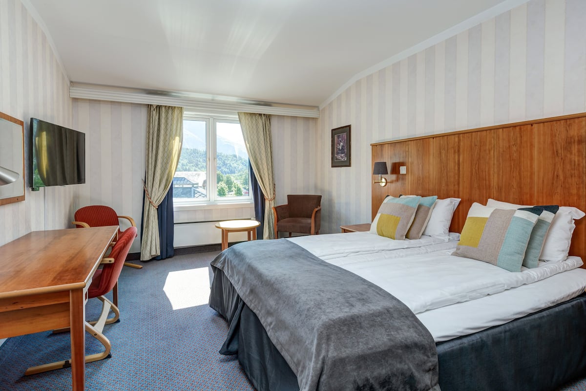 Une chambre d’hôtel avec un grand lit, un bureau, une chaise, une télévision et une fenêtre avec des rideaux.