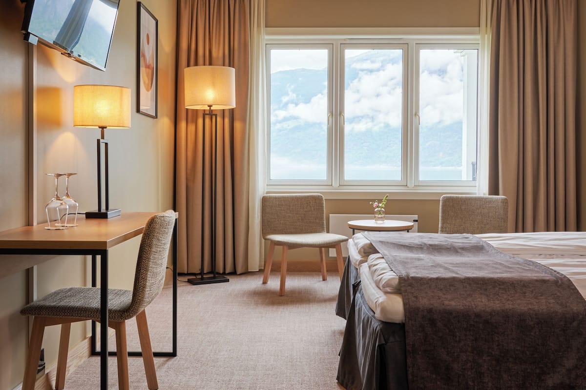 Une chambre d’hôtel équipée d’un lit, d’un bureau, d’une chaise, d’une télévision, d’une lampe et d’une fenêtre avec des rideaux.