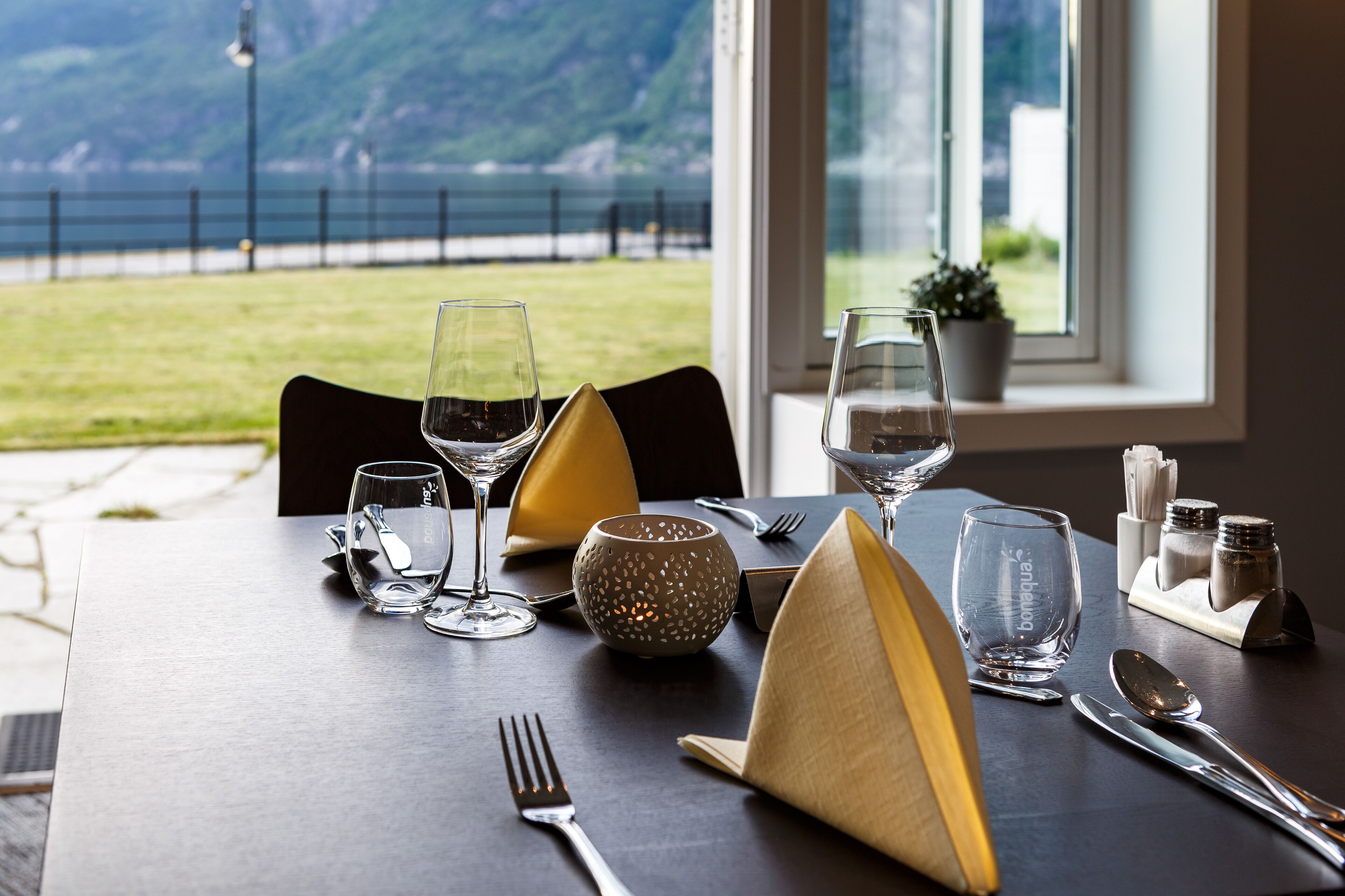 Een eettafel gedekt met wijnglazen, een schaal, bestek en uitzicht op zee.