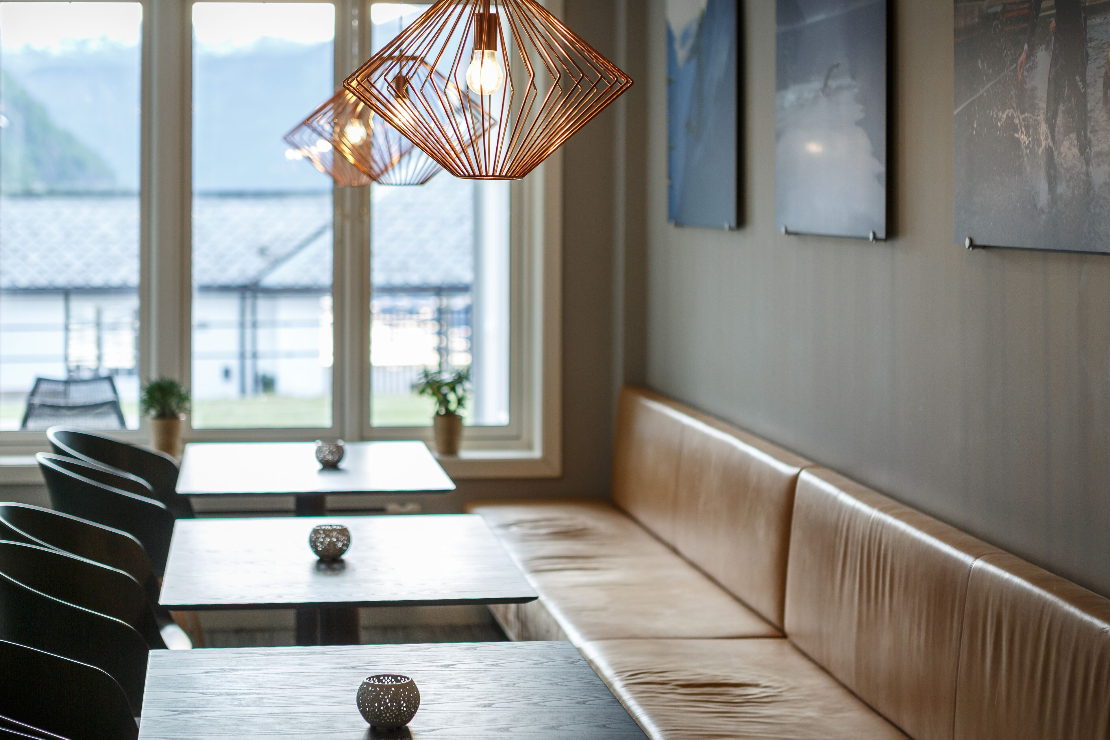 Interior de restaurante con banco de madera, mesas e iluminación colgante.