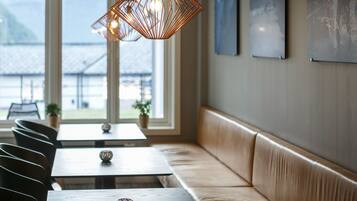 Interior de restaurante con banco de madera, mesas e iluminación colgante.