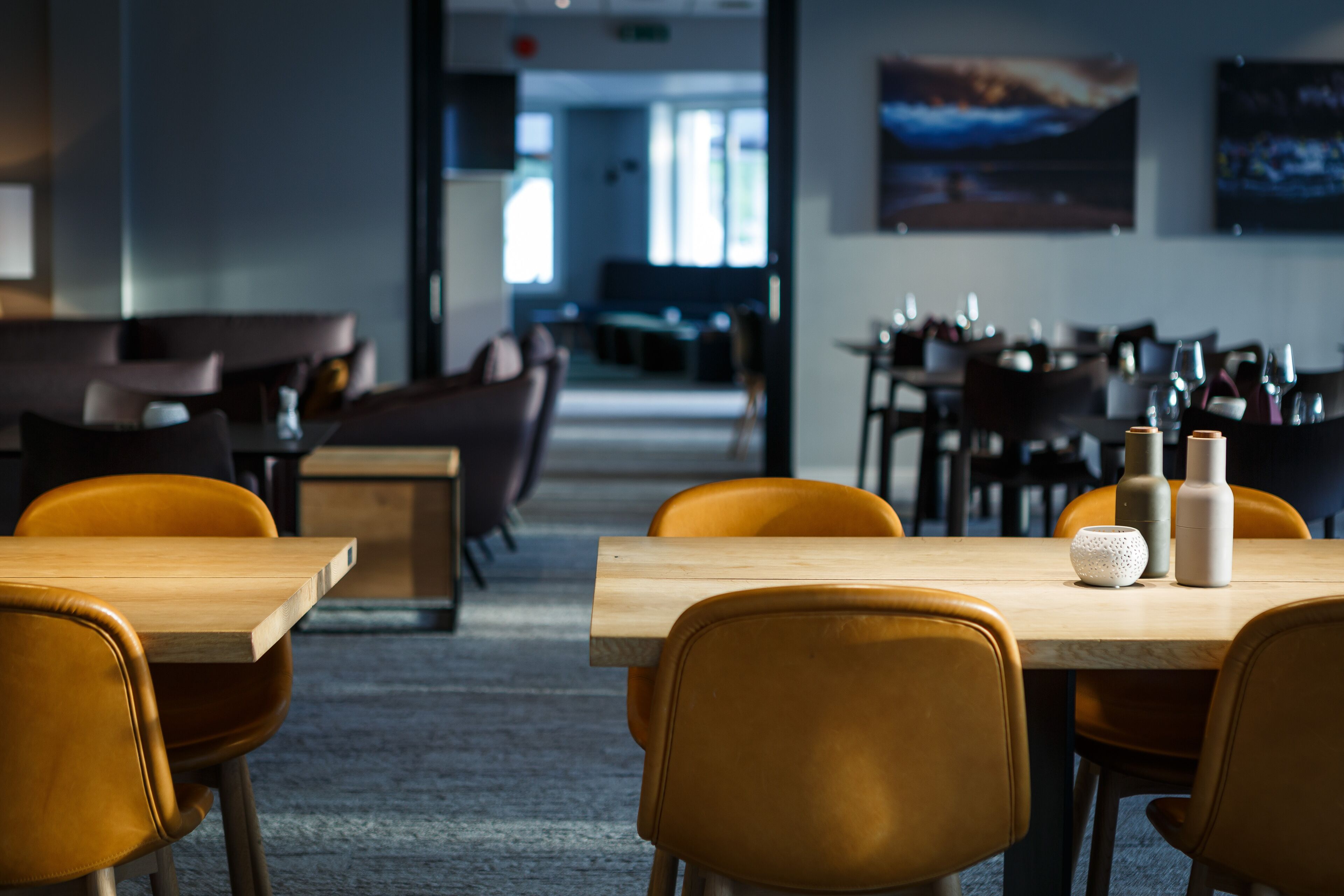 A modern dining area with wooden tables and orange chairs, featuring a view of the dining area in the background.