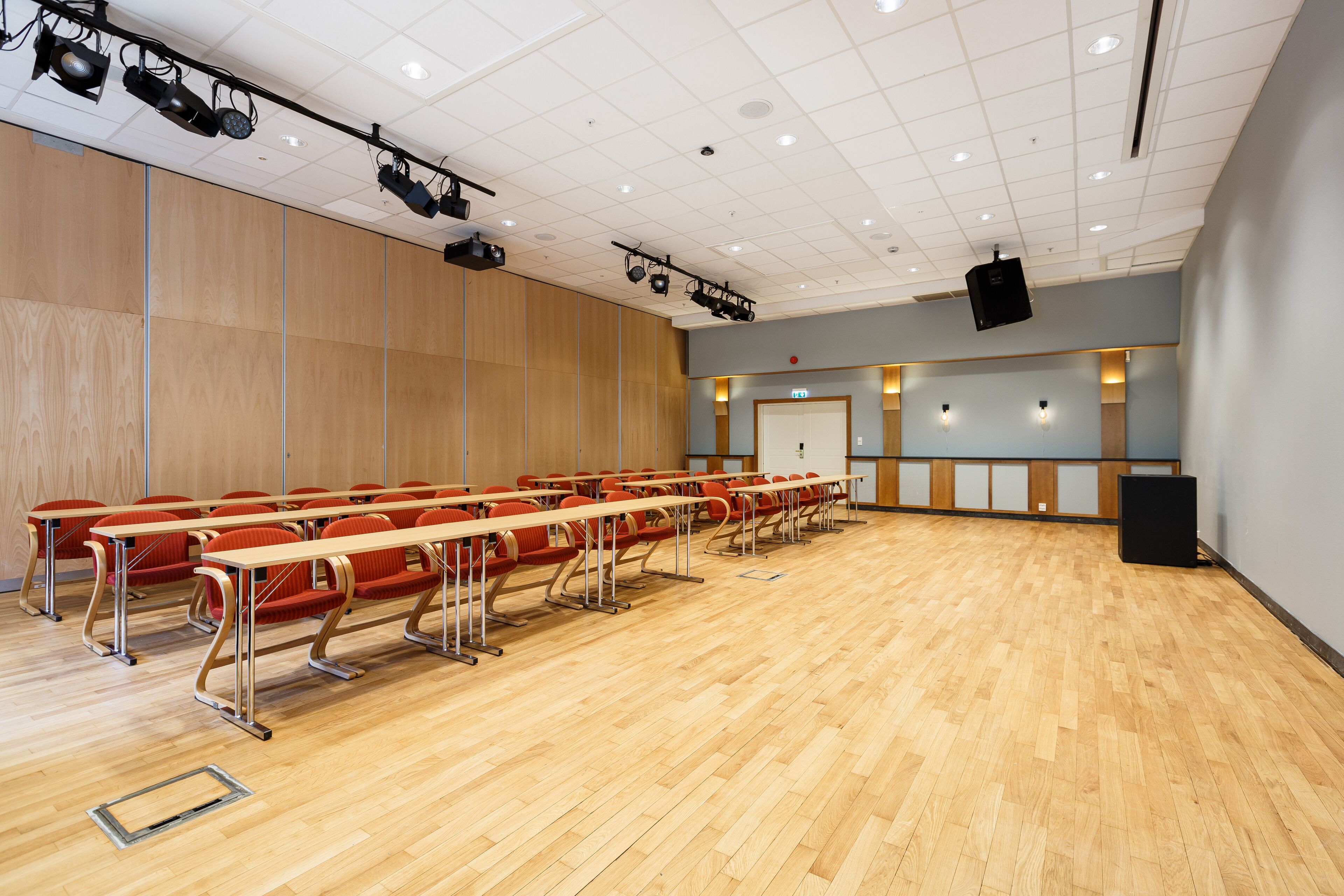 A conference room with rows of chairs, a stage with lighting, and a wooden floor.