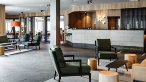 Un hall d’hôtel moderne avec un comptoir d’accueil, un espace salon et un restaurant en arrière-plan.