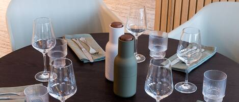 Een ronde eettafel gedekt met verschillende wijnkannen, een kaars en bestek op een donker houten tafelkleed.