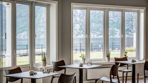 Un espace repas doté de grandes fenêtres donnant sur un lac, avec des tables et des chaises disposées pour les repas.