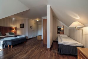 Ett hotellrum med två sängar, ett trägolv, en sänggavel i trä, ett nattduksbord, en lampa och en spegel.