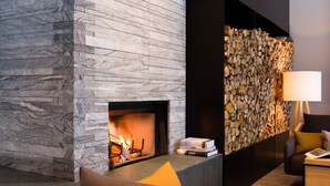 Un intérieur moderne agrémenté d’une cheminée en pierre, d’un mur en bois et d’un coin salon confortable avec une lampe.