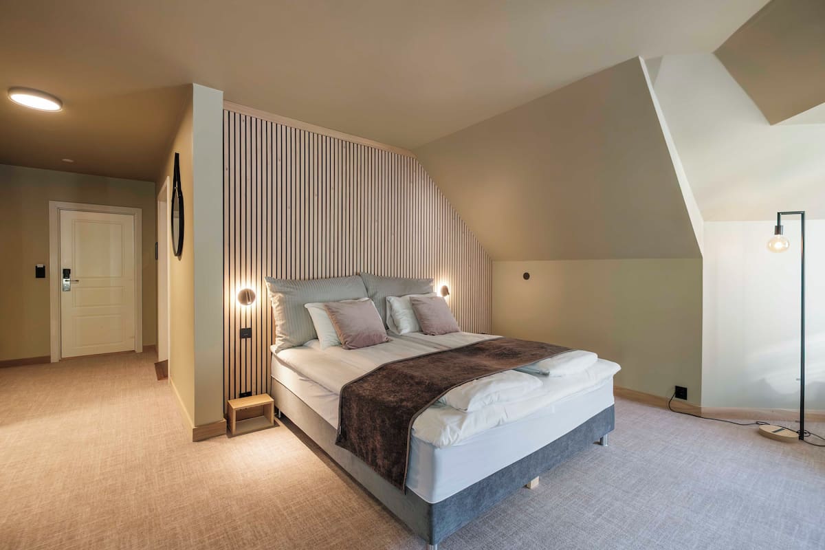Une chambre à coucher comprenant un lit, des tables de chevet, une lampe fixée au mur et un luminaire au plafond.