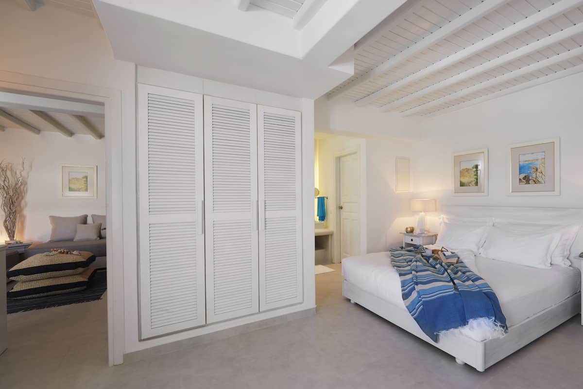 A bedroom with a large bed, a nightstand, a bedside table, a wardrobe, and a bathroom visible through an open door.