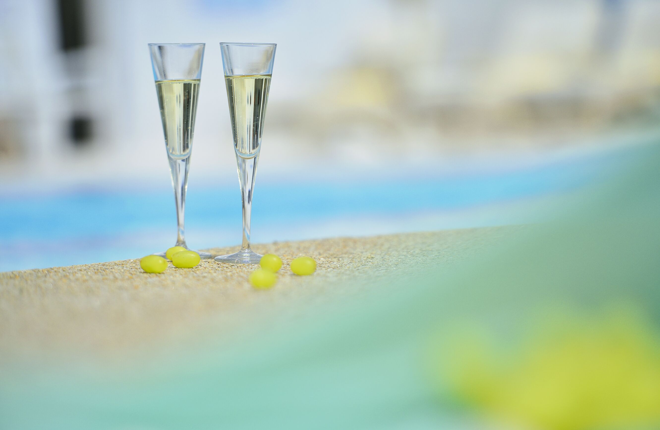Two champagne flutes on a sandy surface with a blurred background.