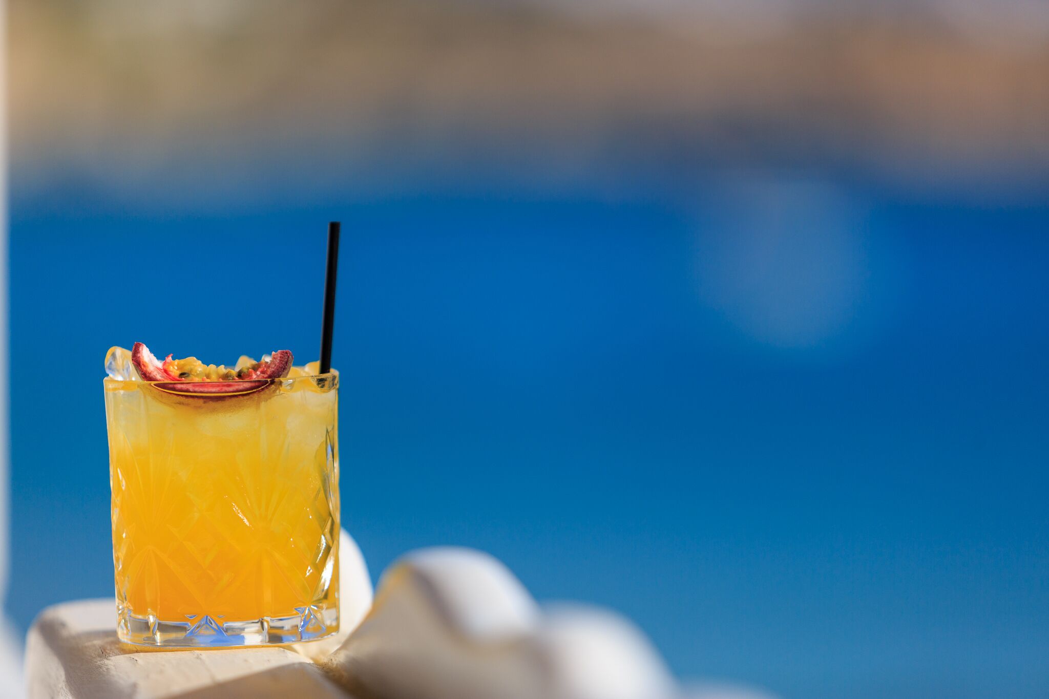 Ein Cocktail mit Fruchtscheibe und Trinkhalm auf einer weißen Oberfläche vor blau verschwommenem Hintergrund.