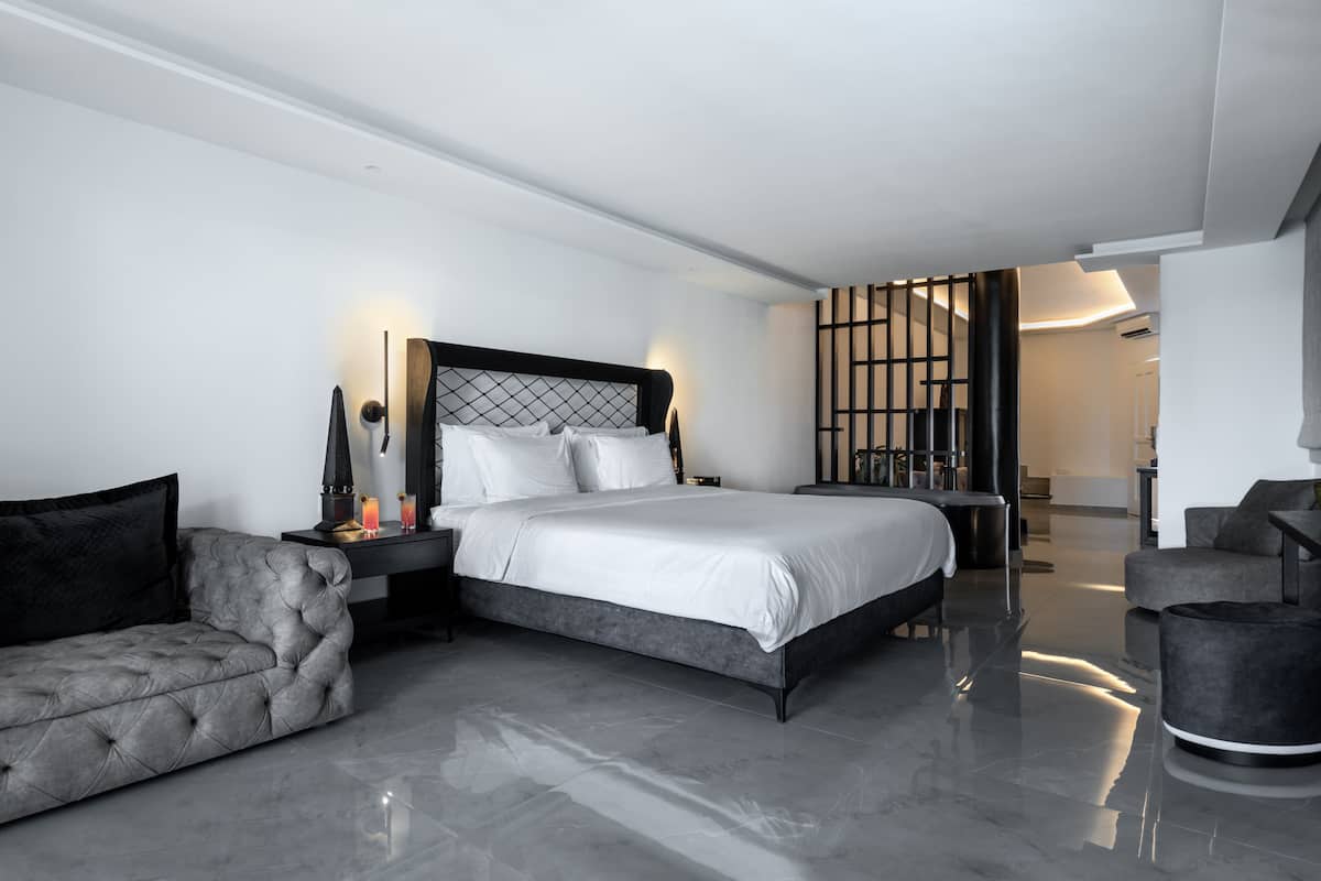 A modern bedroom with a large bed, a grey sofa, and a small table with a lamp.
