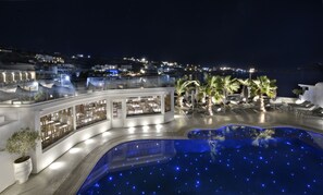 A nighttime view of a resort with a pool, palm trees, and a bar area. - Petinos Beach Hotel (Mykonos)
