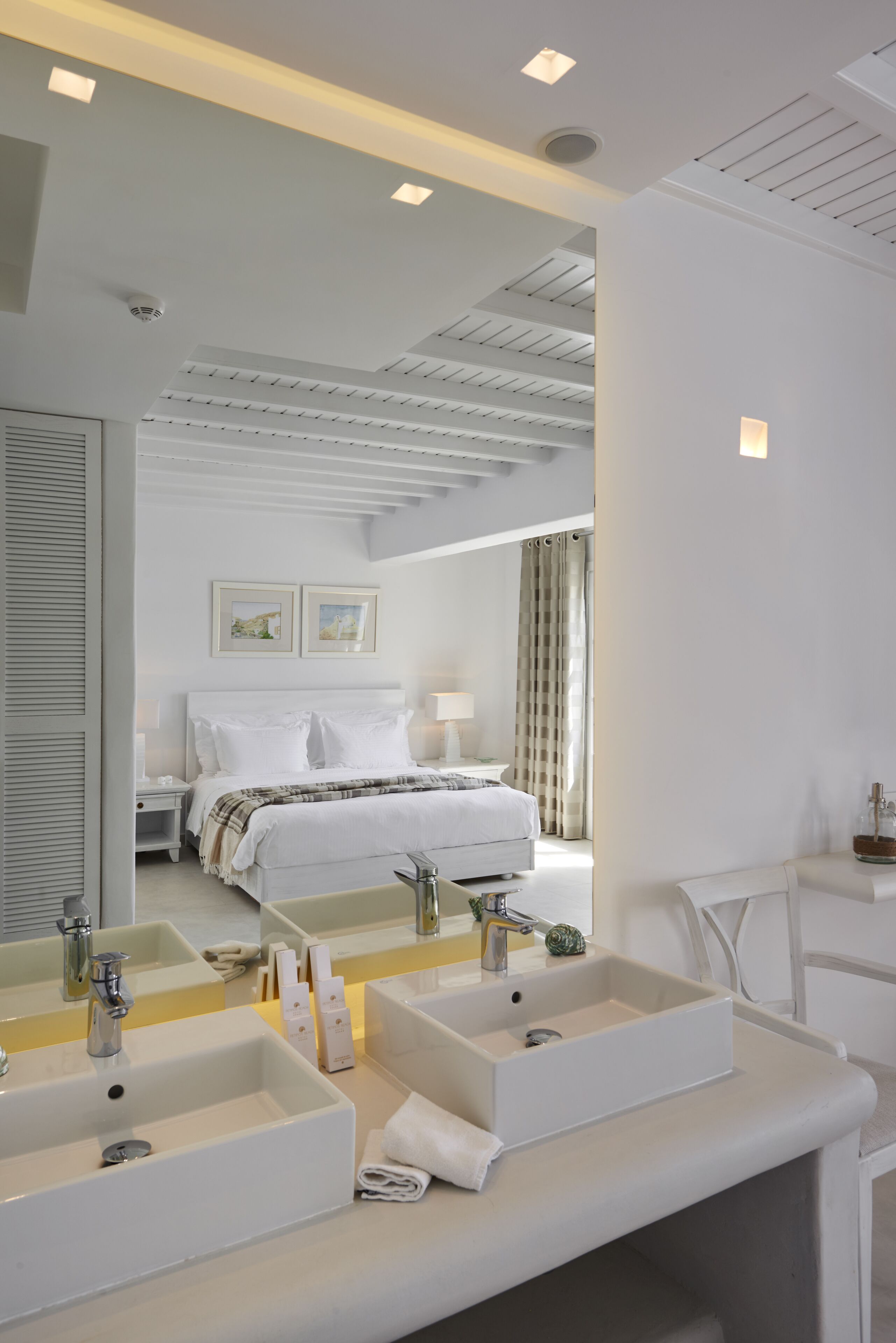 A modern hotel room with a large bed, two bedside tables, a double sink, and a mirror.