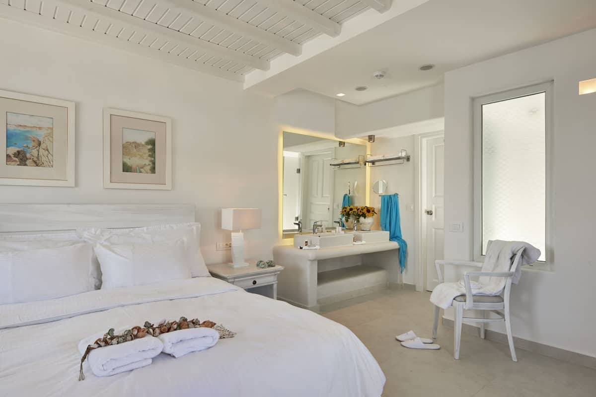 A hotel room with a large bed, a bathroom with a sink and mirror, and a chair.