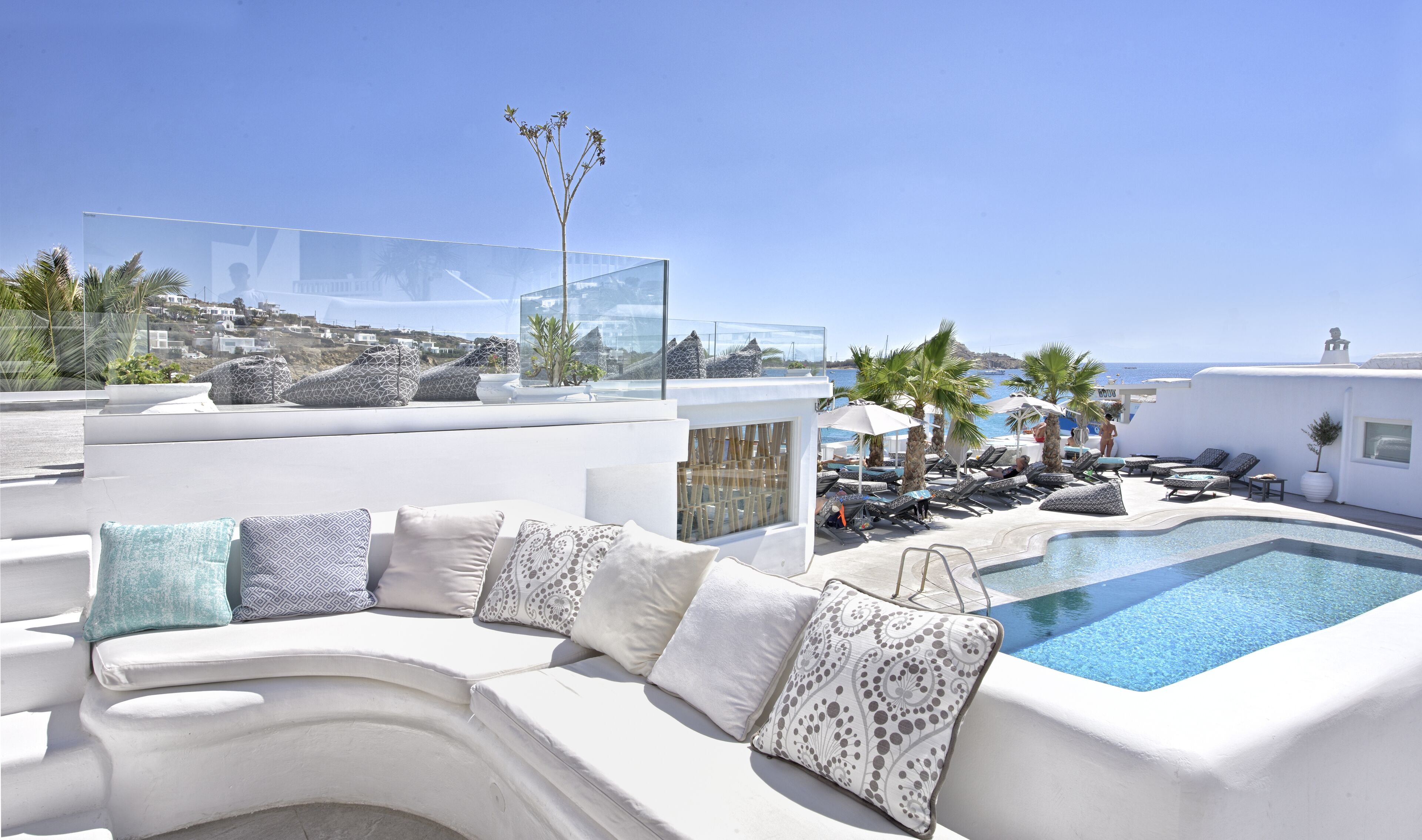 A white infinity pool with lounge chairs and a white sofa with patterned cushions.