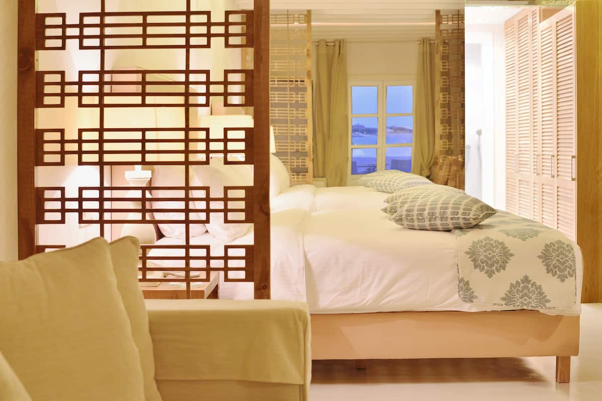 A bedroom with a bed, a chair, and a view of the sea through a window.