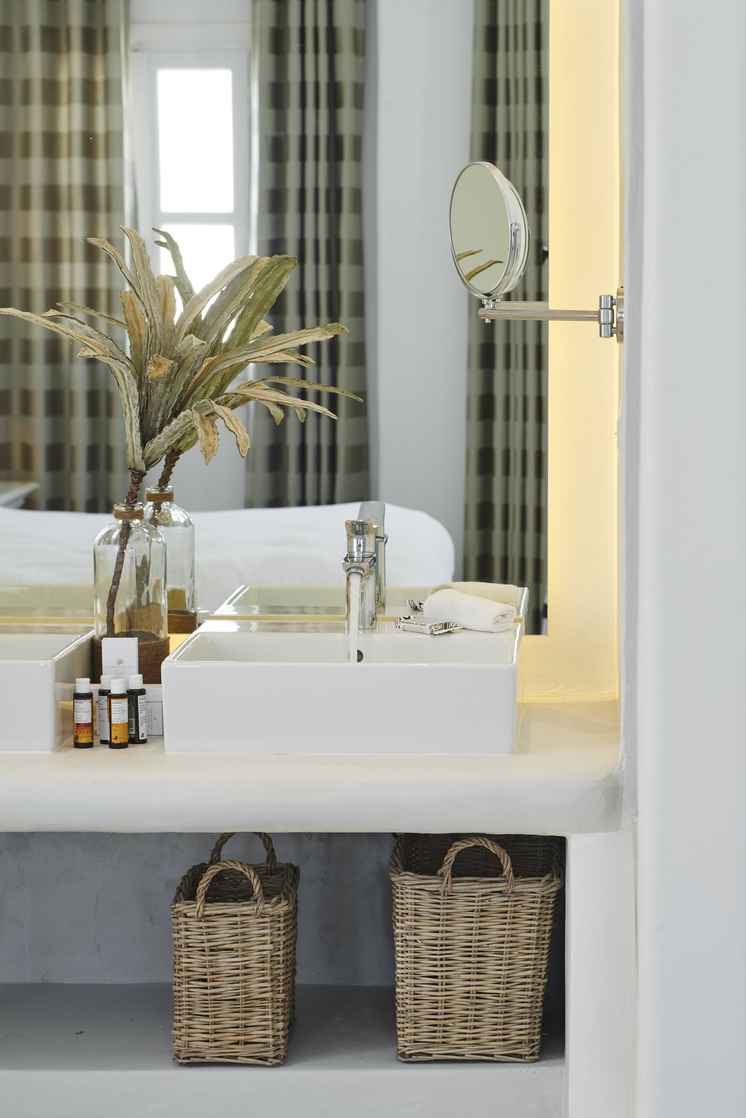 Un baño con un lavabo blanco, un espejo, una planta y dos cestas de mimbre.
