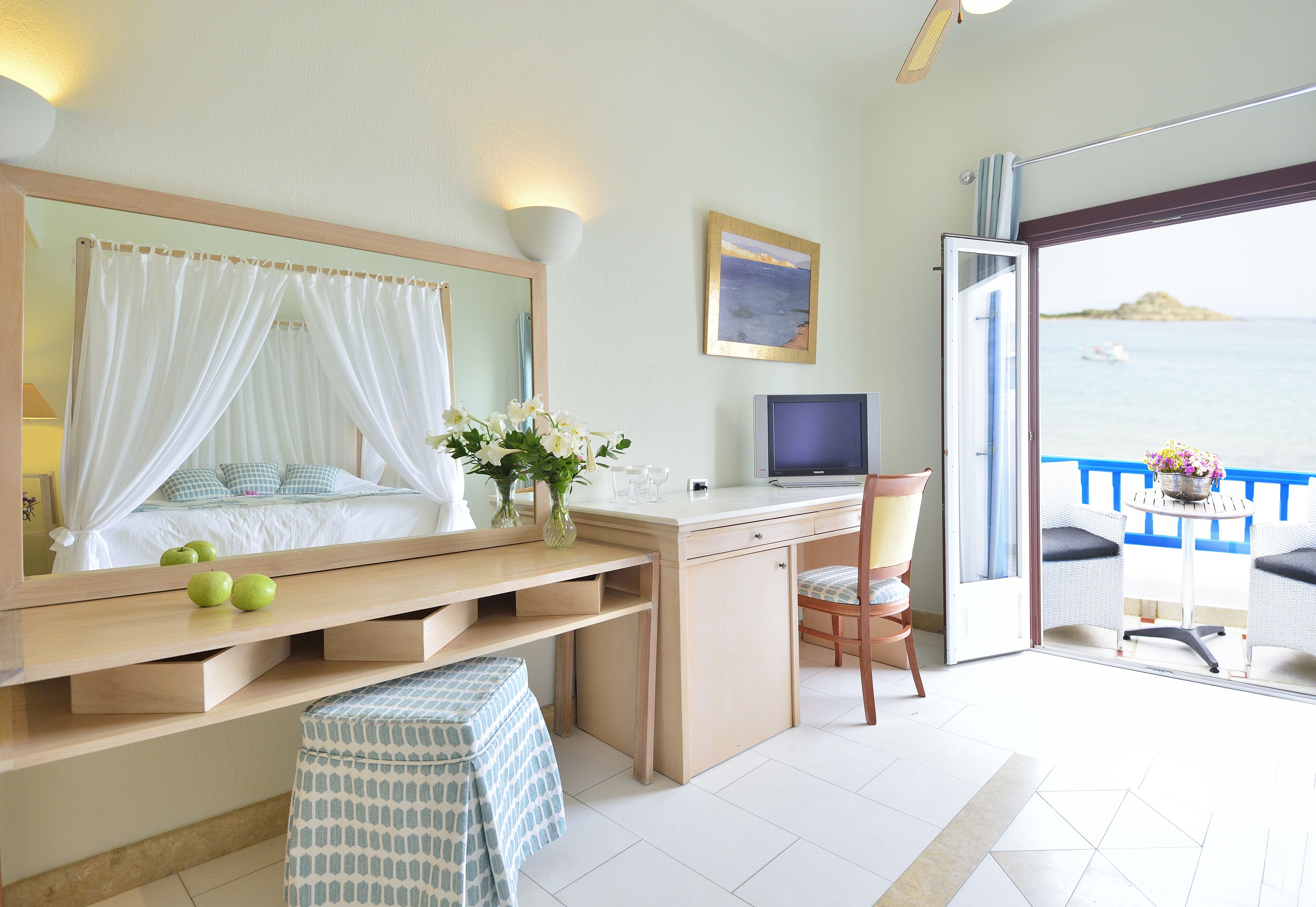 A bedroom with a bed, bedside table, TV, and a balcony with a view of the sea.