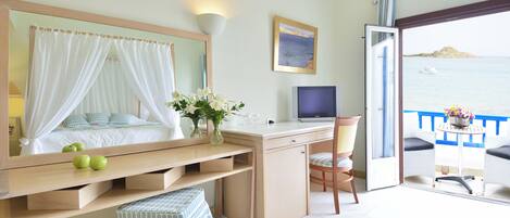 A bedroom with a bed, bedside table, TV, and a balcony with a view of the sea.