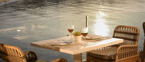 A table set for two with wine glasses and a small plant, overlooking a calm body of water.