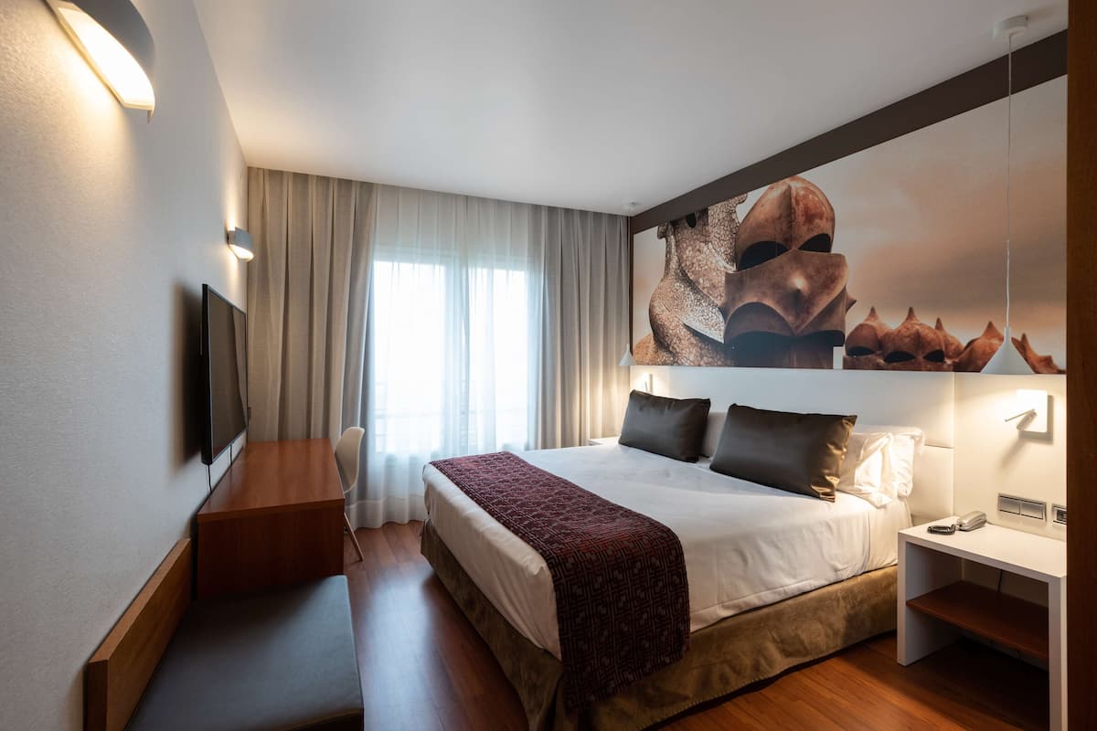 A hotel room with a large bed, a bedside table, a TV, and a wall-mounted artwork.