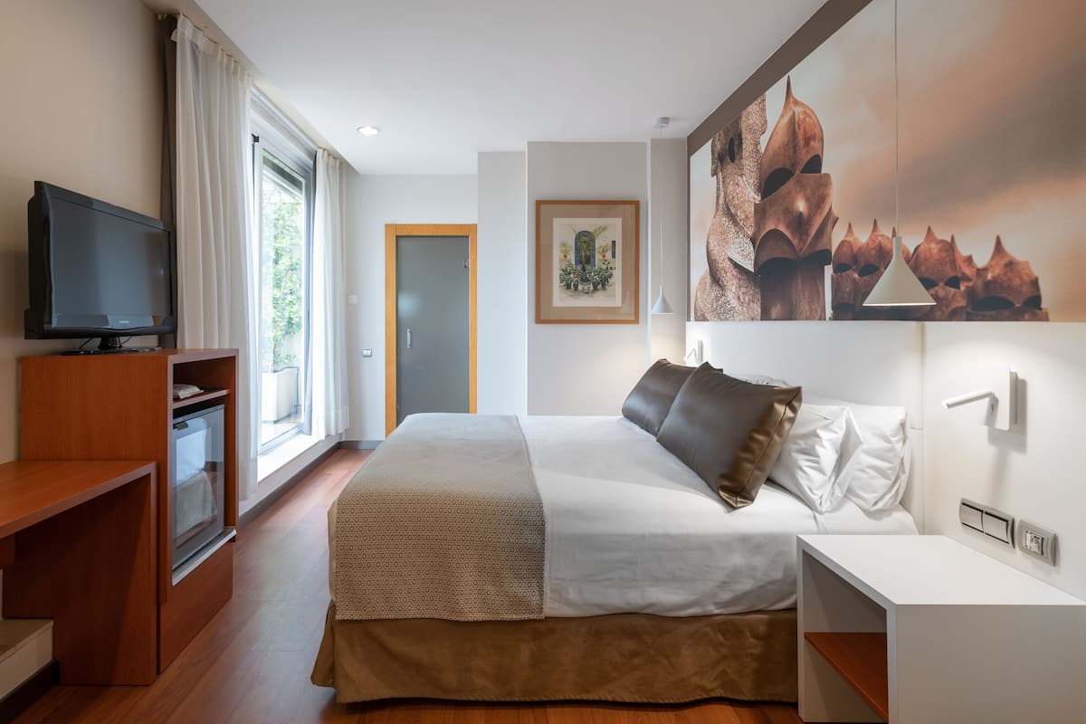 A modern hotel room with a large bed, a television, a desk, and a window with curtains.
