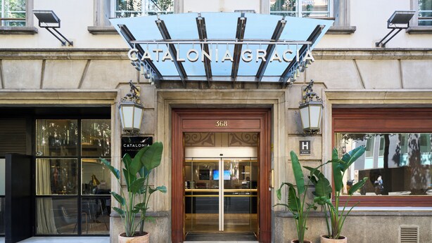 La entrada de un hotel con puerta de vidrio, plantas en macetas y un letrero sobre la puerta.