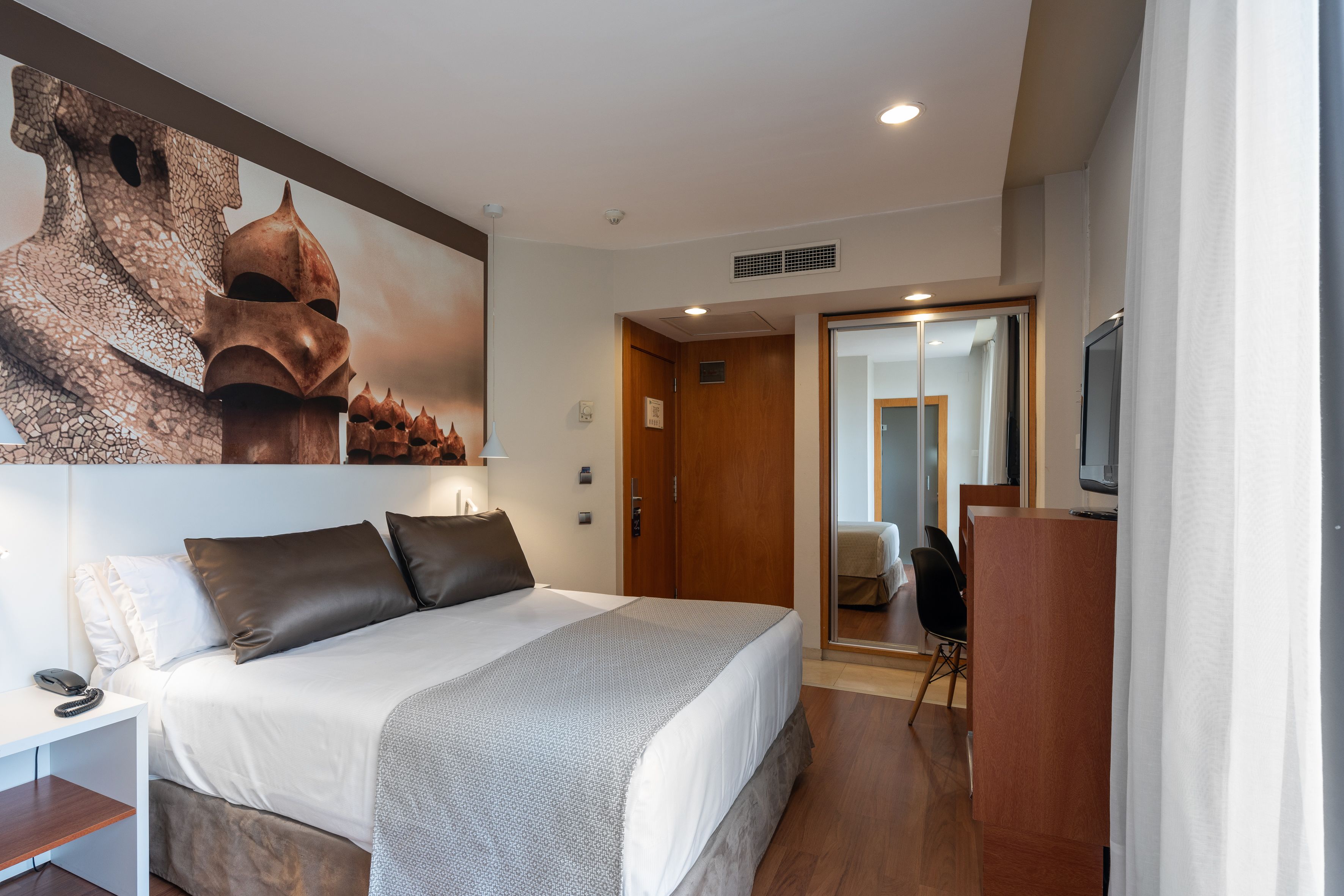 A hotel room with a large bed, a desk, a chair, and a television.