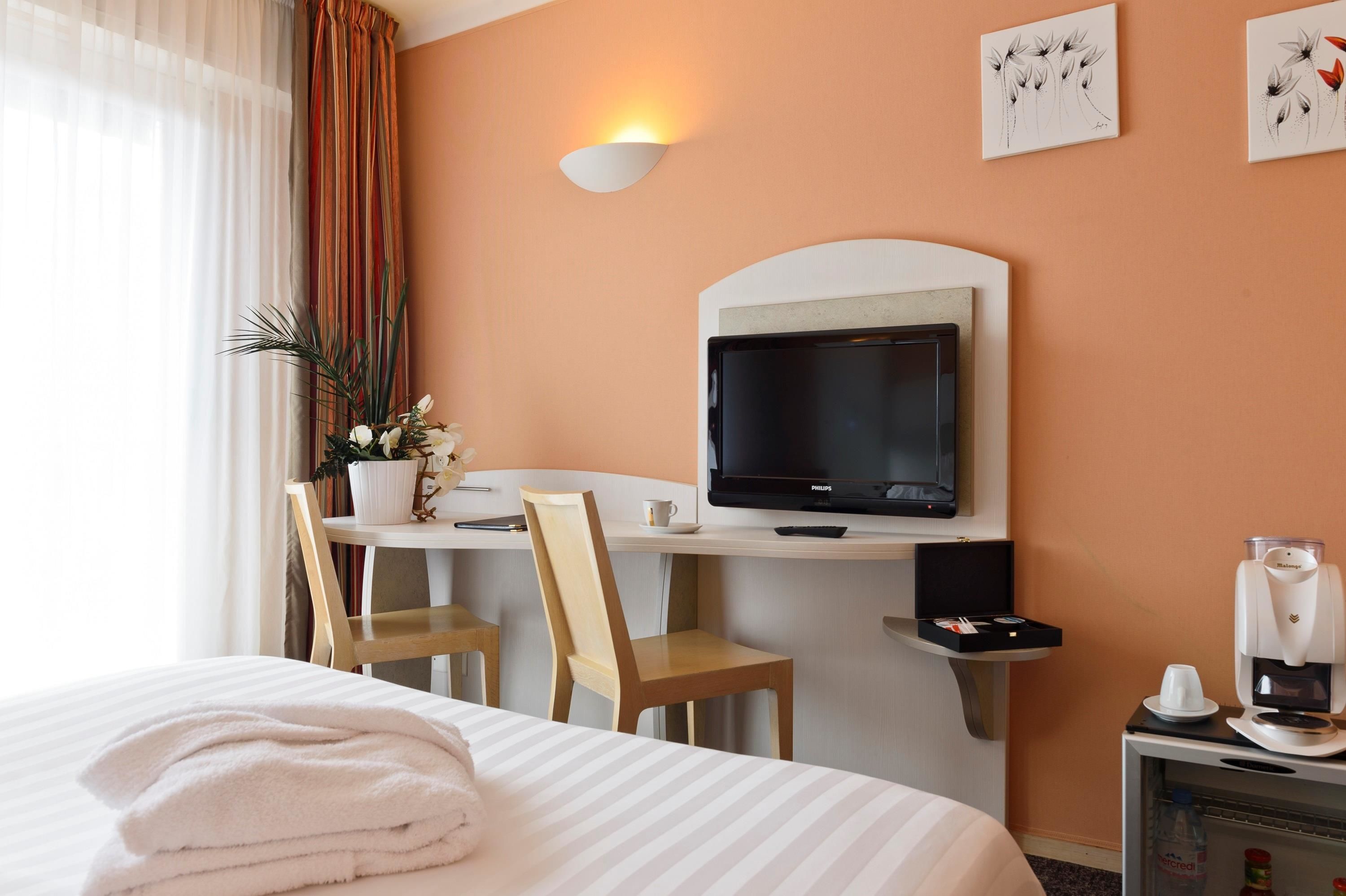 Habitación de hotel con una cama, un escritorio con televisor, una cafetera y una planta.