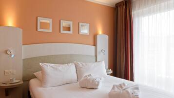 A hotel room with a bed, white bedding, a nightstand with a cup and remote, and a window with curtains.