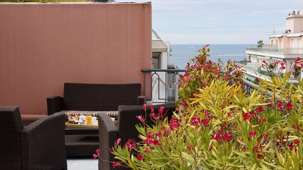 A balcony with wicker furniture, a tray with food, and a view of the sea. - Best Western Astoria (Antibes)