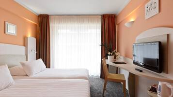 A hotel room with two beds, a desk with a TV, a chair, a bedside table, and a window with curtains.