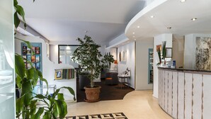 A modern hotel lobby with a reception desk, potted plants, a patterned rug, and a seating area. - Best Western Astoria (Antibes)