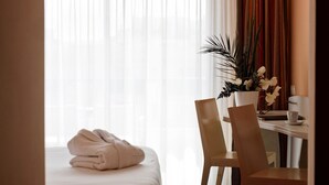 A hotel room with a bed, a desk with a chair, a vase of flowers, and a window with sheer curtains. - Best Western Astoria (Antibes)