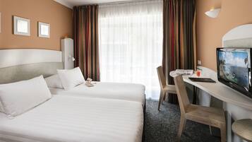 Une chambre d’hôtel avec deux lits, un bureau équipé d’un ordinateur et d’une télévision, et une fenêtre avec des rideaux.