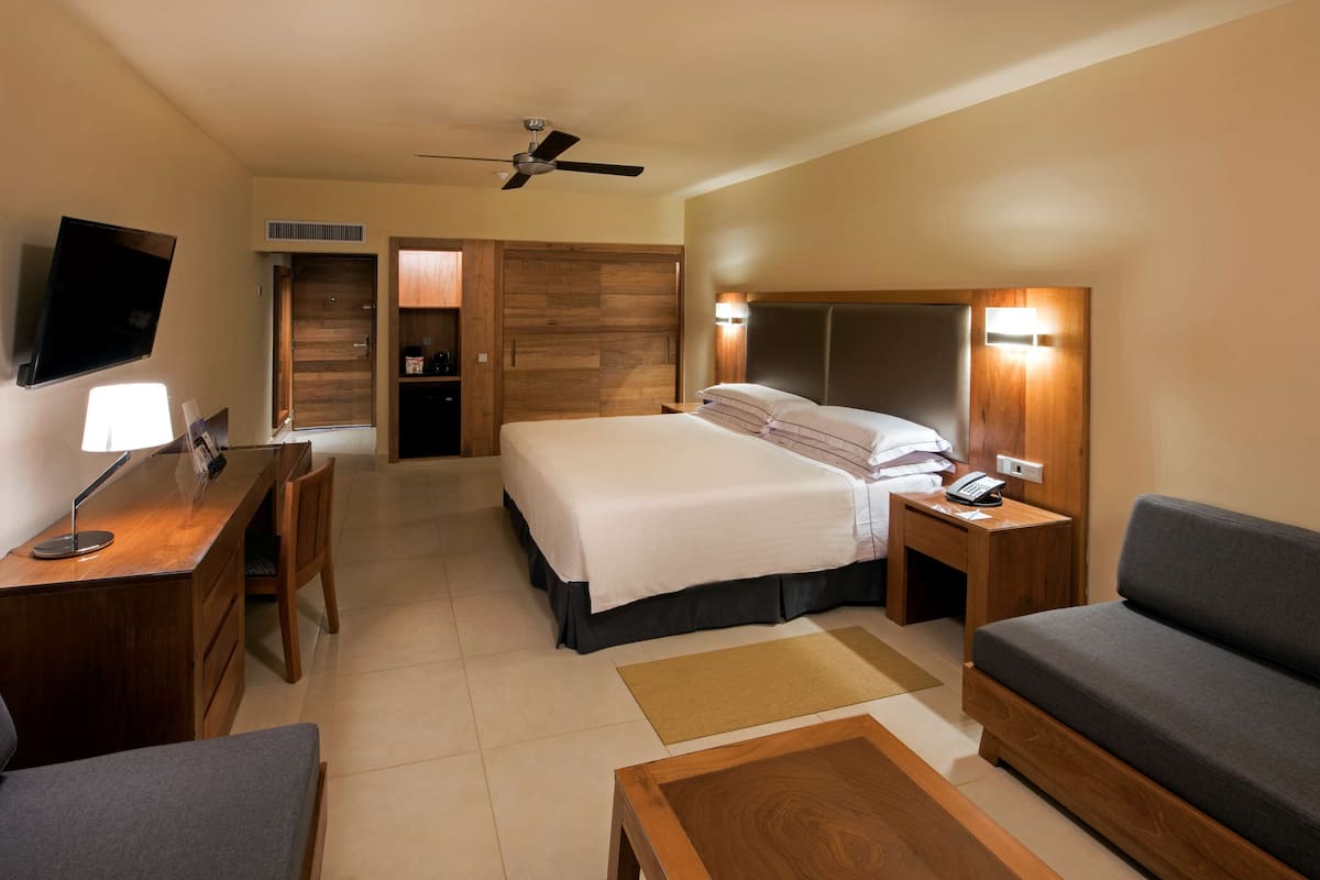 A hotel room with a bed, a desk, a chair, a sofa, a TV, and a ceiling fan.