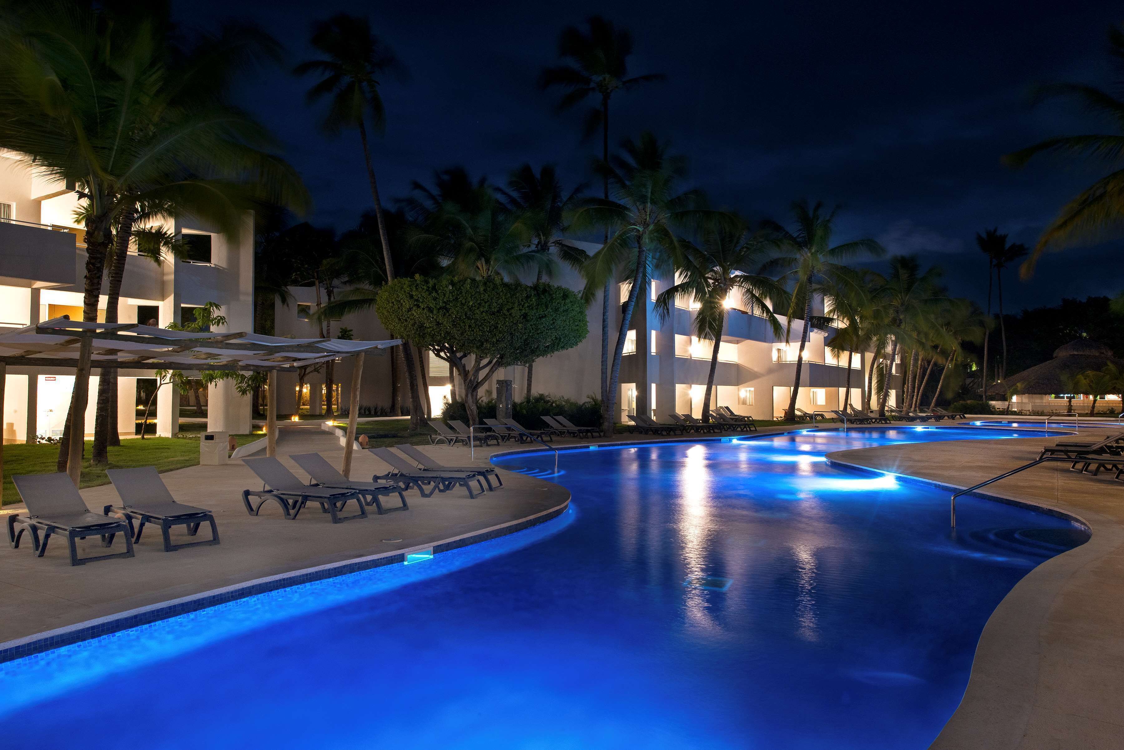 Una piscina con sillones de descanso y palmeras de noche.